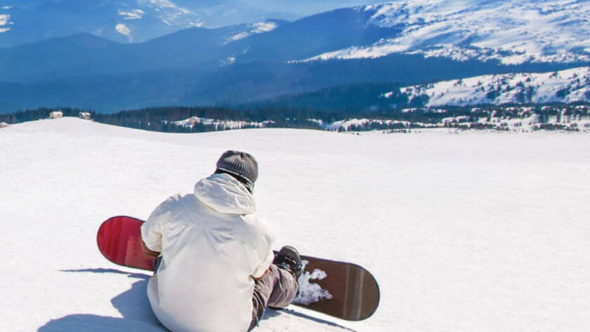 Snowboarder sitting at top of mountain, looking over horizon