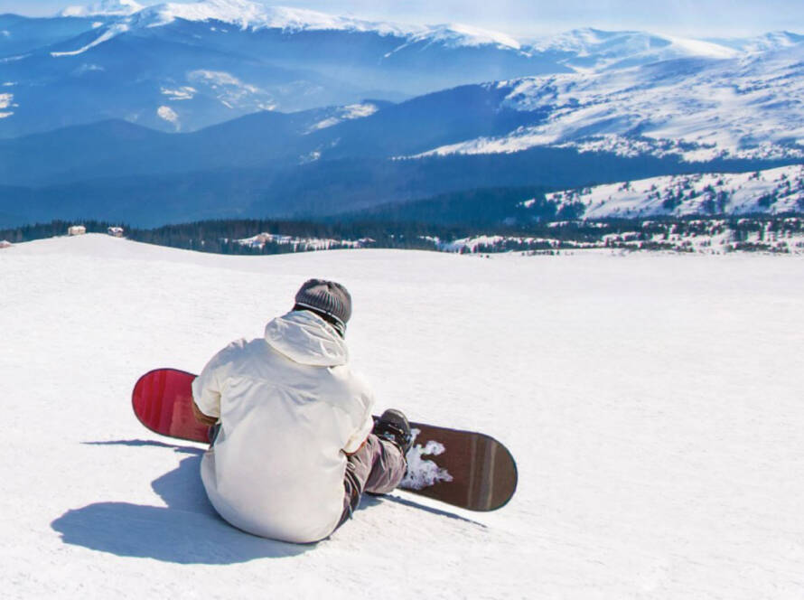 Snowboarder sitting at top of mountain, looking over horizon