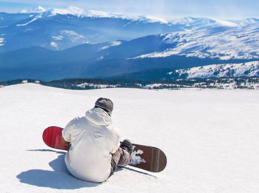 Snowboarder sitting at top of mountain, looking over horizon