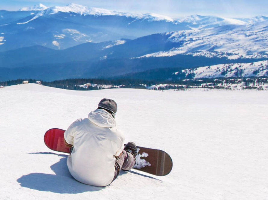 Snowboarder sitting at top of mountain, looking over horizon