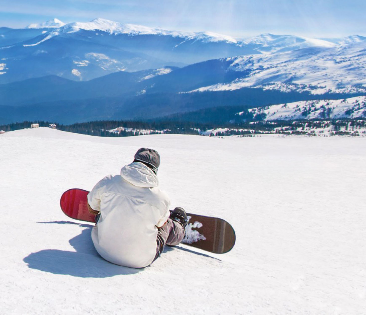 Snowboarder sitting at top of mountain, looking over horizon