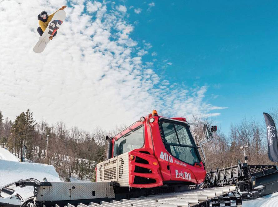 Snowboarder jumping over snow grooming machine
