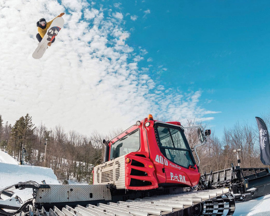 Snowboarder jumping over snow grooming machine