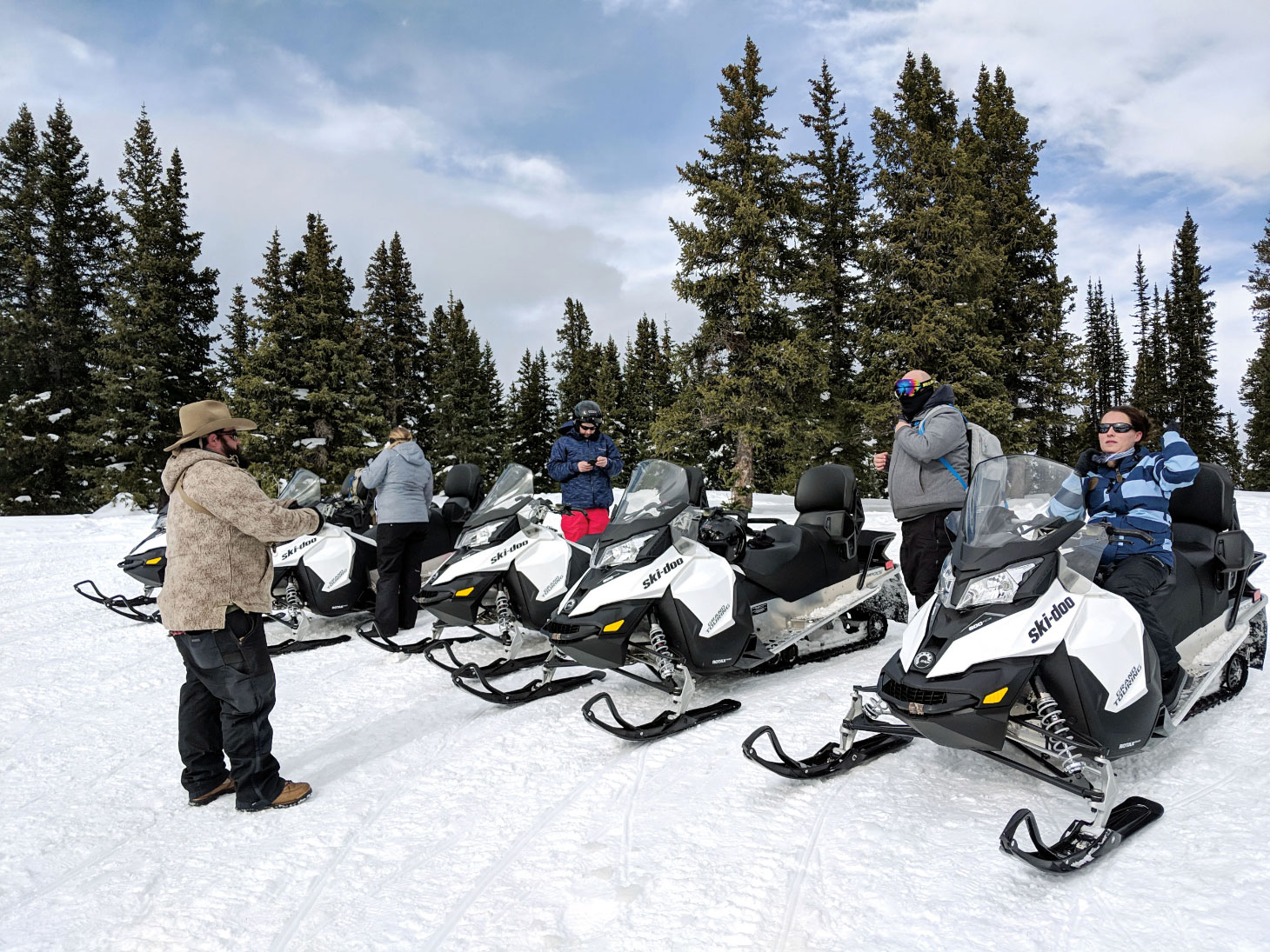 Snowmobilers on snowmobiles with trees in background