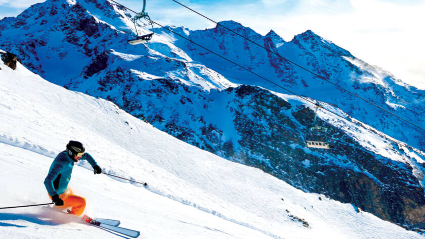 Skier skiing down slope with mountains in background.