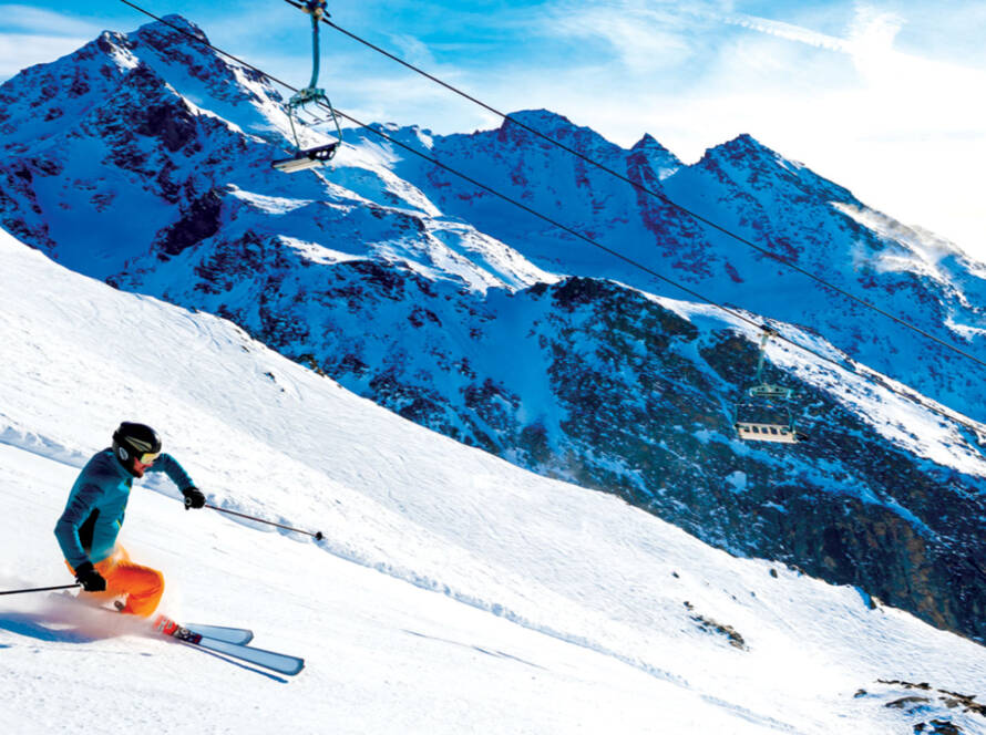 Skier skiing down slope with mountains in background.