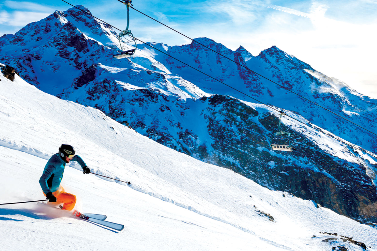 Skier skiing down slope with mountains in background.