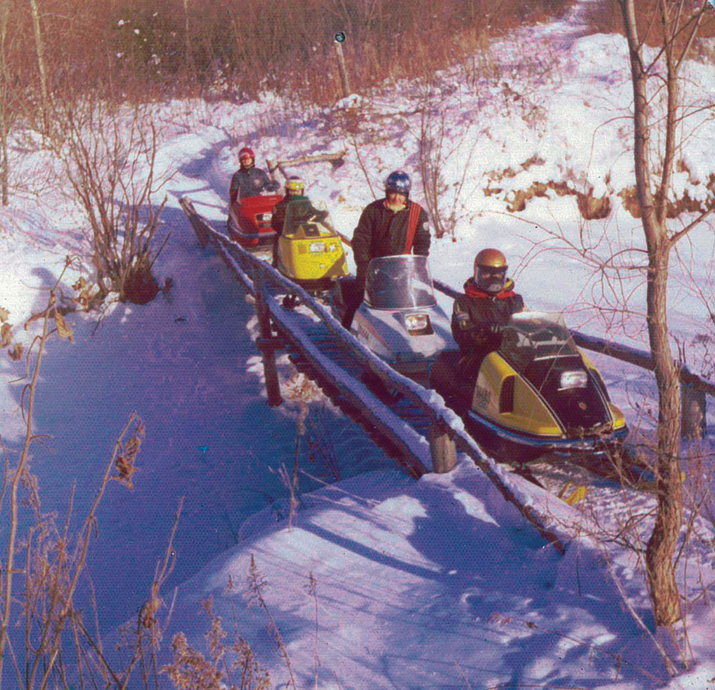 Photo of riders on snowmobiles on footbridge