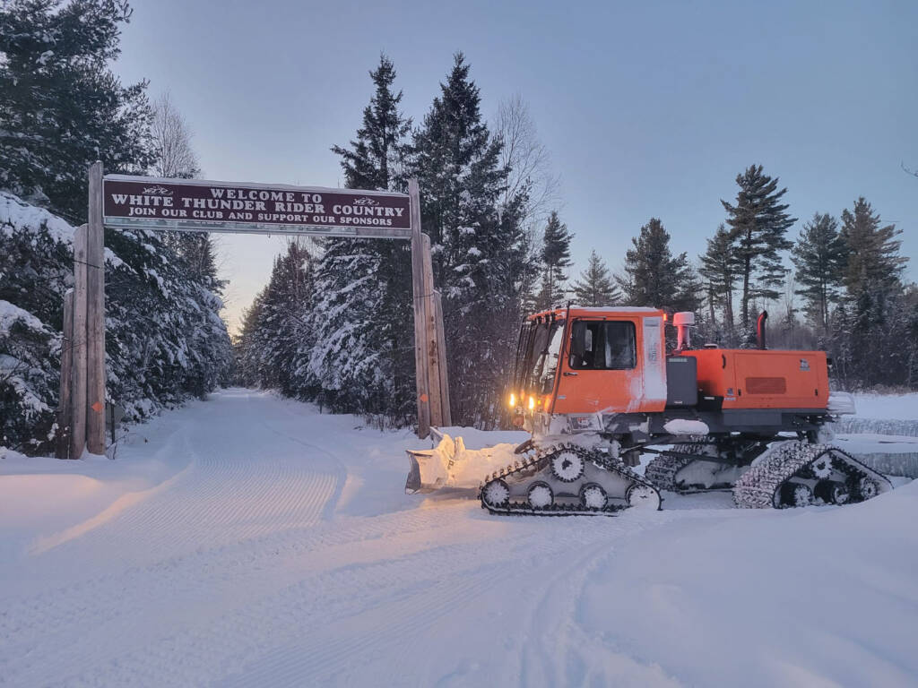 Sno-Cat with lights on in front of Welcome to White Thunder Rider Country sign.