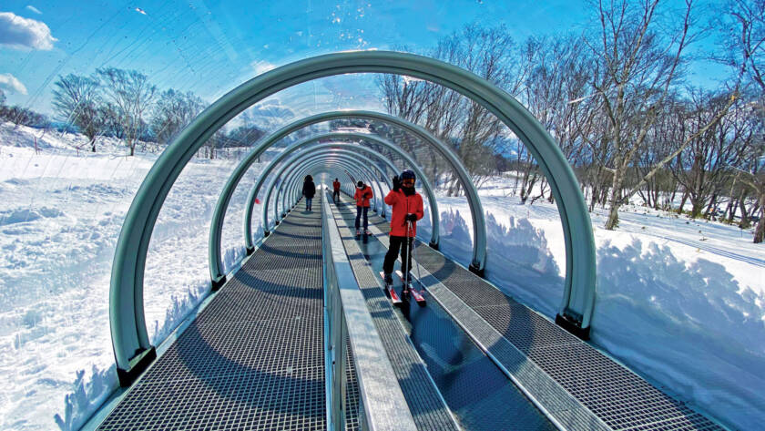 Skiers in a covered conveyor belt ski lift