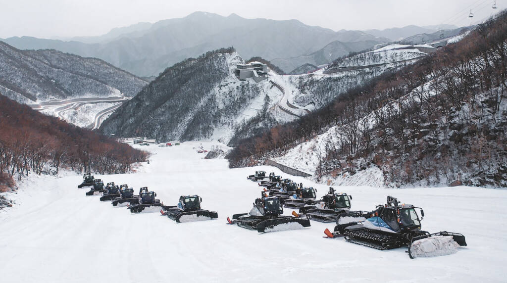 Calvary of snow grooming machines ascending mountain