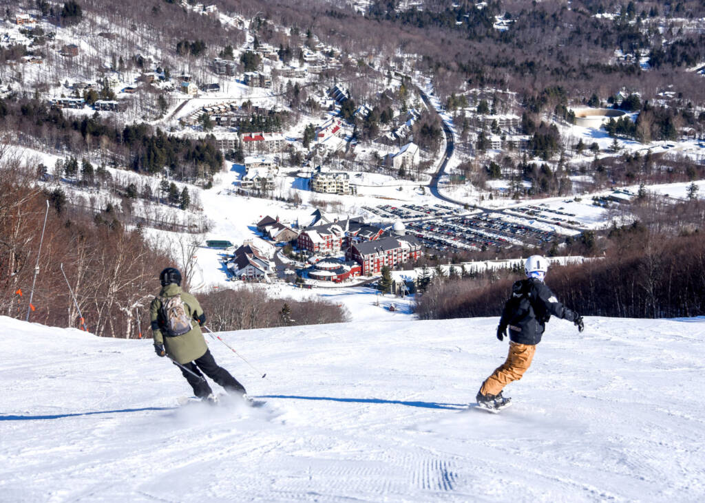 Skier and snowboarder heading downhill toward resort