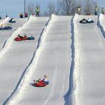 Adults and children going down ski slope in tubes