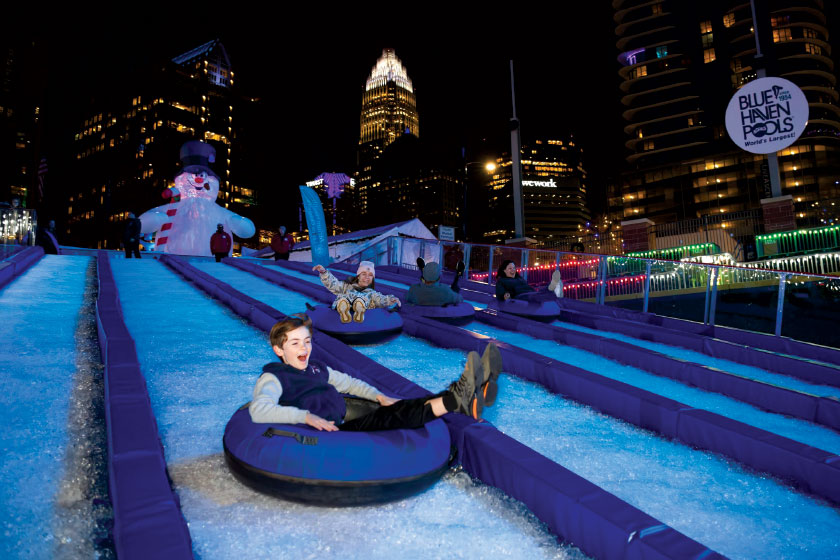 Adults and children going down ski slopes in tubes at night