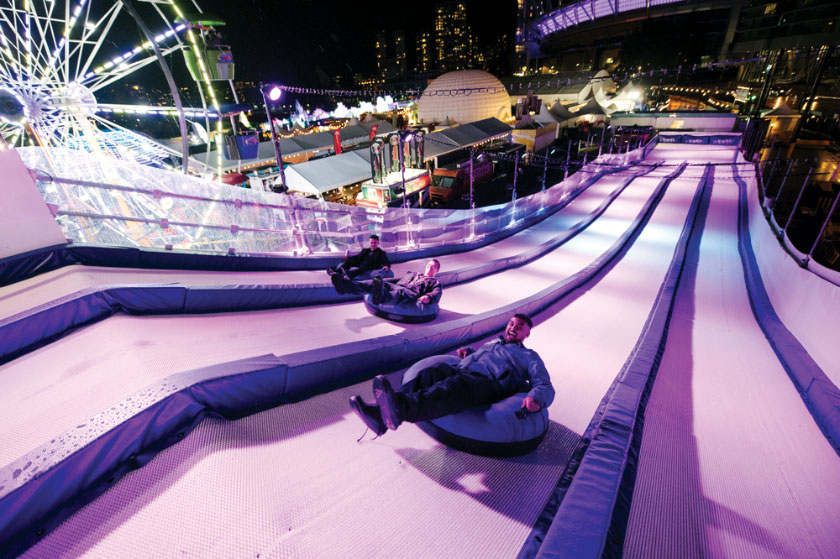 Adults and children going down ski slope in tubes at night