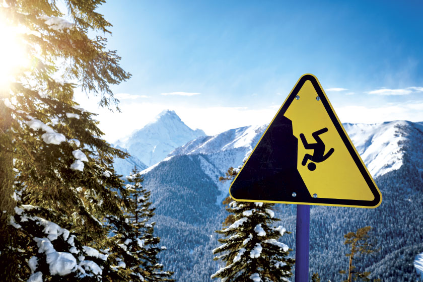 Yellow warning sign on the edge of the ski slope in mountains