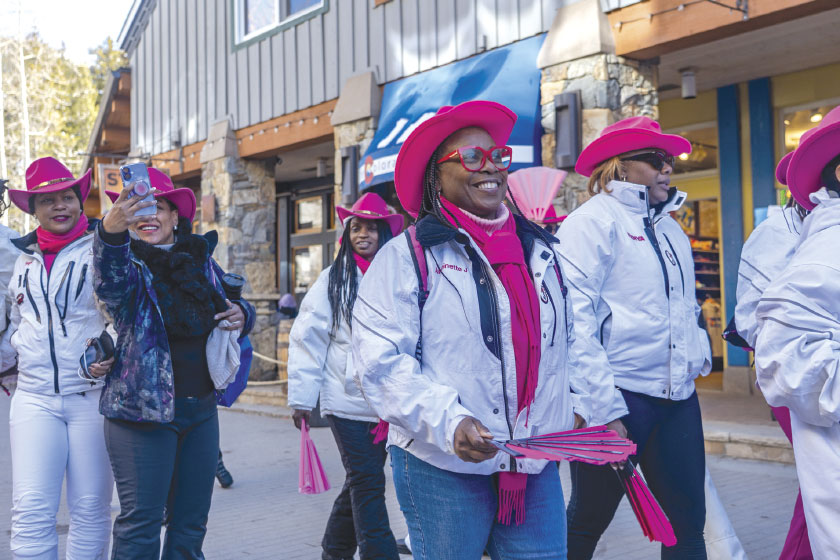 Group in matching white team jackets, pink hats and scarfs parade in streets