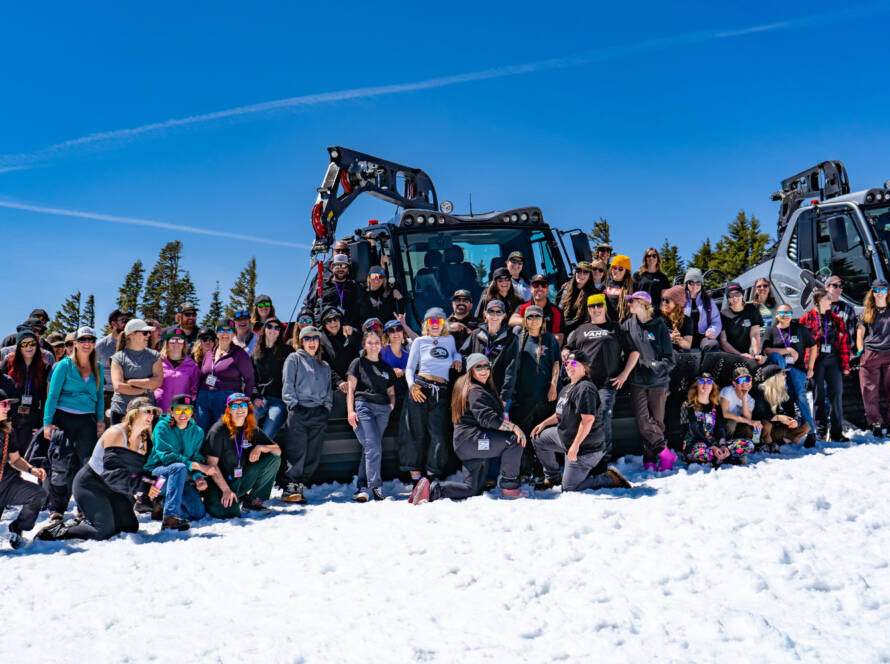 Large group posing for photo in front of snow grooming machine
