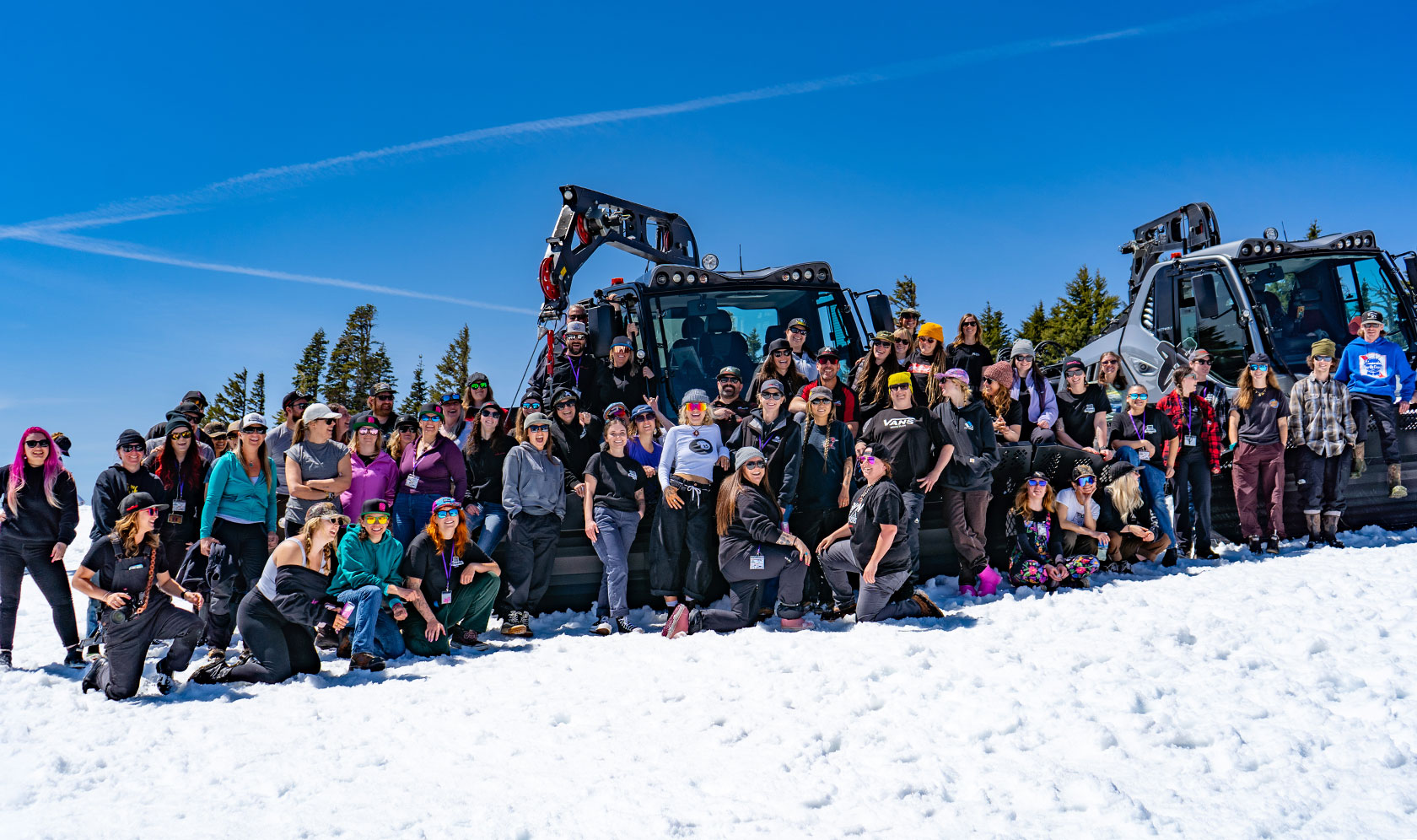 Large group posing for photo in front of snow grooming machine