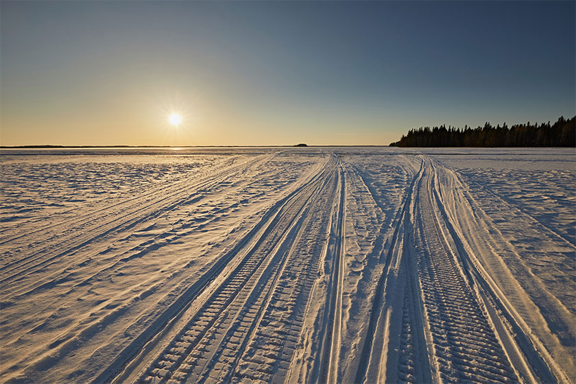 Snowmobile tracks in the snow against a sunset sky