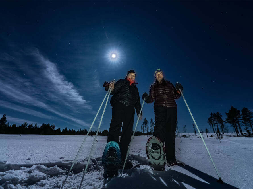 Couple in snowshoes at night under full moon