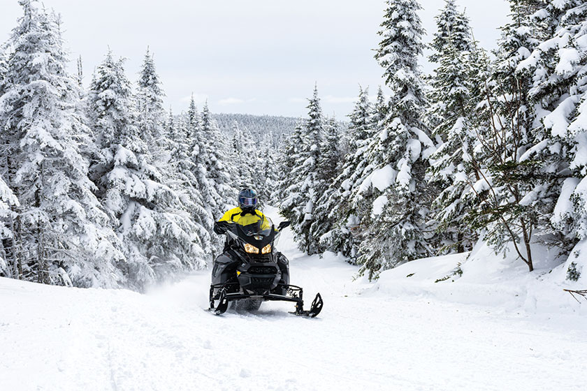 Snowmobiler riding on a trail in the forest on a cold winter day