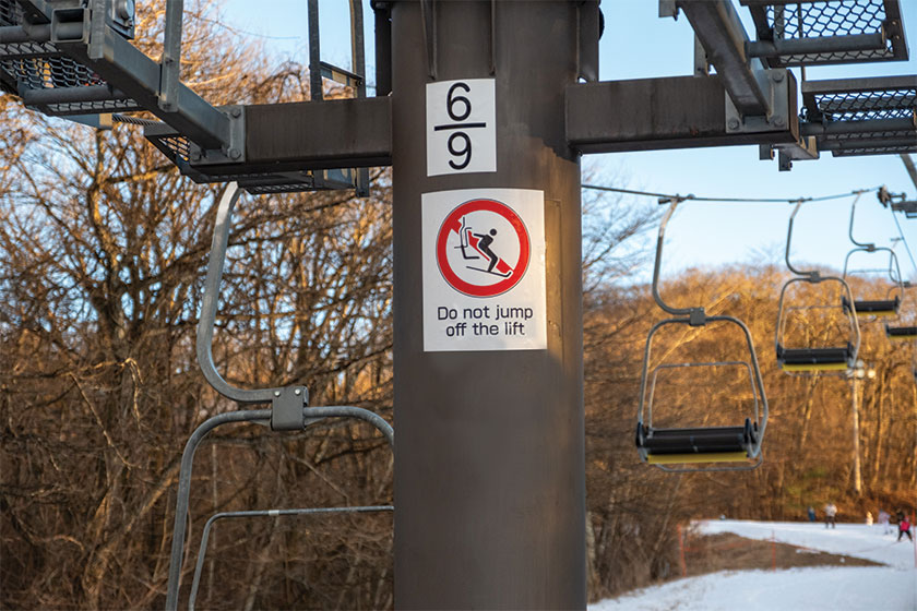 Warning sign on ski lift support tower cautioning against jumping from chair at Karuizawa Ski Resort, December 16, 2024, Karuizawa, Japan